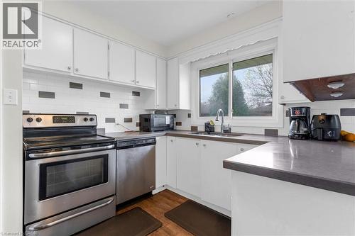 Kitchen featuring white cabinetry, a subway tile backsplash with accent tiles, stainless steel appliances, dark countertops, and wood-finish flooring - 46 Beaconsfield Drive, Hamilton, ON - Indoor Photo Showing Kitchen