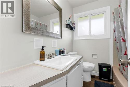 Bathroom featuring a vanity with a white countertop and integrated sink, a large framed mirror, a privacy window, a toilet, and wood-finish flooring - 46 Beaconsfield Drive, Hamilton, ON - Indoor Photo Showing Bathroom