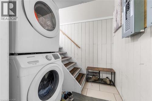 Dedicated laundry area featuring a stacked washer and dryer, white paneled walls, a neutral-toned tiled floor, and a wooden handrail along the adjacent staircase - 46 Beaconsfield Drive, Hamilton, ON - Indoor Photo Showing Laundry Room
