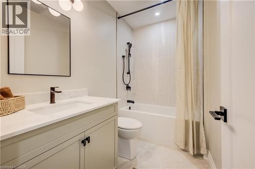 Bathroom featuring a light-toned vanity with a built-in sink, dark bronze hardware, a framed mirror, and a full bathtub with a tiled surround - 210 Heritage Drive Unit# Main, Kitchener, ON - Indoor Photo Showing Bathroom