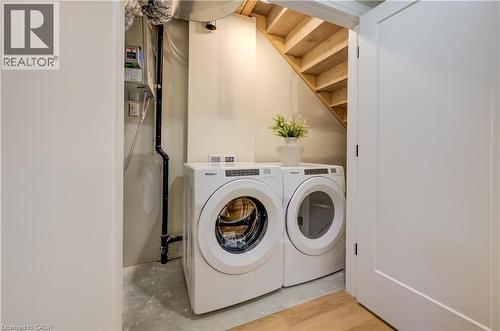 Dedicated laundry area featuring a front-loading washer and dryer, exposed wooden stairwell, and a light wood-finish flooring - 210 Heritage Drive Unit# Main, Kitchener, ON - Indoor Photo Showing Laundry Room
