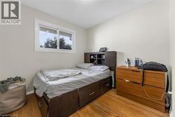 Bedroom featuring light-toned walls, wood-finish flooring, and a white-framed window - 