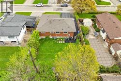 Rear exterior featuring a sizable backyard with a manicured lawn, a paved patio area, and mature trees - 