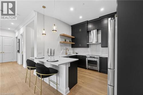 Modern kitchen featuring dark cabinetry, stainless steel appliances, light wood-finish flooring, and a breakfast bar with pendant lighting - 2 Arbourvale Common Unit# 209, St. Catharines, ON - Indoor Photo Showing Kitchen With Upgraded Kitchen