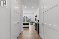 Hallway featuring light wood-finish flooring, recessed lighting, and white paneled doors with brass hardware - 