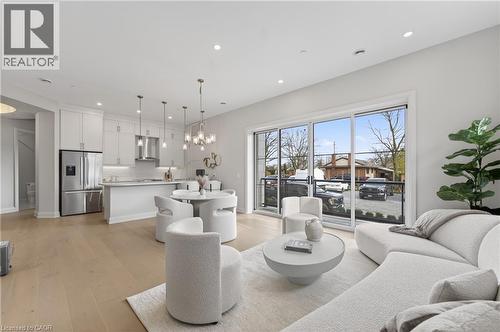 Open-concept living area featuring light wood-finish flooring, recessed lighting, and a modern kitchen with stainless steel appliances - 2 Arbourvale Common Unit# 209, St. Catharines, ON - Indoor Photo Showing Other Room