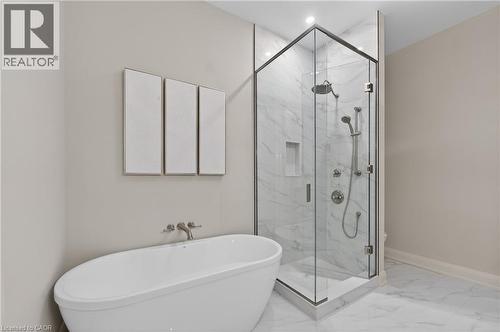 Freestanding soaking tub with wall-mounted brushed nickel faucet, frameless glass shower enclosure with marble-finish tile, and recessed shower niche - 2 Arbourvale Common Unit# 209, St. Catharines, ON - Indoor Photo Showing Bathroom
