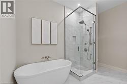 Freestanding soaking tub with wall-mounted brushed nickel faucet, frameless glass shower enclosure with marble-finish tile, and recessed shower niche - 