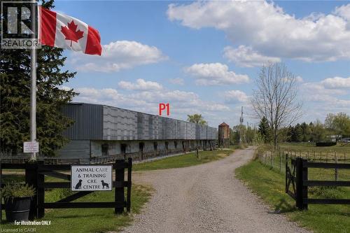 Gravel driveway entry featuring a black wooden fence, a flagpole, and a long industrial-style building - 96 Second Road E, Stoney Creek, ON 