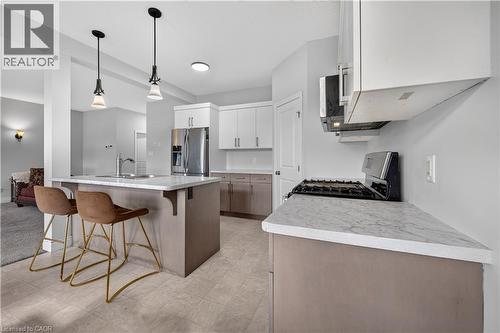 Modern kitchen featuring a central island with integrated sink, stainless steel appliances, white upper cabinetry, and gray lower cabinetry - 32 Ashberry Place, St. Thomas, ON 