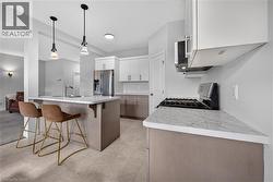 Modern kitchen featuring a central island with integrated sink, stainless steel appliances, white upper cabinetry, and gray lower cabinetry - 