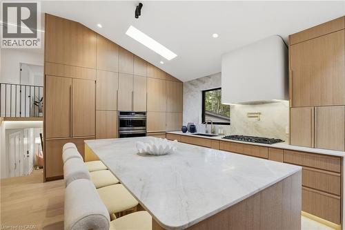 Modern kitchen featuring a large waterfall island with integrated seating, extensive wood-finish cabinetry, built-in double ovens, and a gas cooktop with a pot filler - 345 Rankin Drive, Burlington, ON - Indoor
