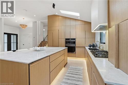Contemporary kitchen featuring extensive light wood cabinetry, a large center island with a stone countertop, built-in appliances, a gas range with a modern hood, and wood-finish flooring with integra - 345 Rankin Drive, Burlington, ON - Indoor Photo Showing Kitchen