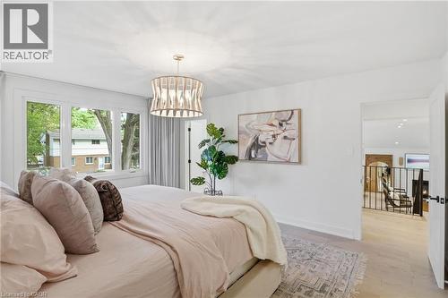 Spacious room featuring light wood-finish flooring, a contemporary chandelier, a large window with white trim, and a wide entryway to an adjacent area - 345 Rankin Drive, Burlington, ON - Indoor Photo Showing Bedroom