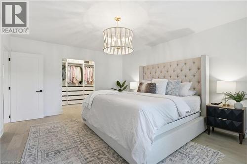 Spacious bedroom featuring light wood-finish flooring, a contemporary chandelier, a built-in custom closet system, and a white paneled door with matte black hardware - 345 Rankin Drive, Burlington, ON - Indoor Photo Showing Bedroom