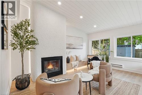 Living area featuring a textured white fireplace surround with a black-framed insert, recessed lighting, wood-finish flooring, and a slat-paneled ceiling - 345 Rankin Drive, Burlington, ON - Indoor Photo Showing Living Room With Fireplace
