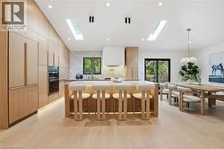 Kitchen and dining area featuring light wood-finish cabinetry, a large center island with integrated seating, stone countertops, and wood-finish flooring - 