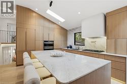 Modern kitchen featuring a large waterfall island with integrated seating, extensive wood-finish cabinetry, built-in double ovens, and a gas cooktop with a pot filler - 