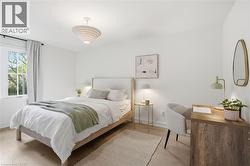Bedroom featuring light wood-finish flooring, a white window frame, and a contemporary ceiling light fixture - 