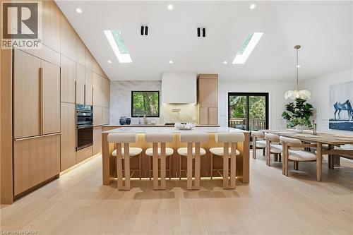 Kitchen and dining area featuring light wood-finish cabinetry, a large center island with integrated seating, stone countertops, and wood-finish flooring - 345 Rankin Drive, Burlington, ON - Indoor Photo Showing Dining Room