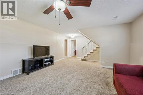 Carpeted living area featuring a ceiling fan with integrated lighting, neutral wall tones, and a visible staircase with white balusters - 47 Oakhurst Crescent, Kitchener, ON - Indoor