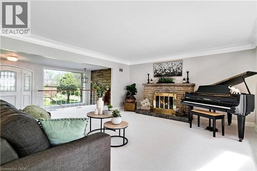 Living area featuring a stone-clad fireplace with a brass firebox, white carpeting, and crown molding - 91 Limerick Drive, Kitchener, ON - Indoor With Fireplace