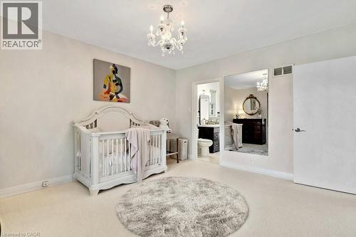 Carpeted room with a crystal chandelier, white walls, and an open doorway leading to an attached bathroom - 91 Limerick Drive, Kitchener, ON - Indoor Photo Showing Bedroom