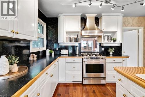 Kitchen featuring white cabinetry, dark countertops, hardwood flooring, stainless steel range with matching range hood, and track lighting - 91 Limerick Drive, Kitchener, ON - Indoor Photo Showing Kitchen