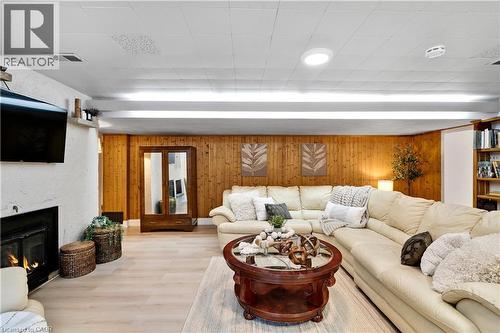 Spacious common area featuring wood-finish flooring, wood panel accent wall, white textured fireplace, and built-in shelving - 91 Limerick Drive, Kitchener, ON - Indoor Photo Showing Living Room With Fireplace