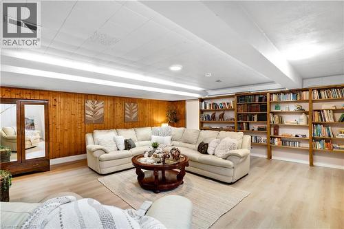 Recreation room featuring wood paneling, extensive built-in shelving, wood-finish flooring, and a drop ceiling with integrated strip lighting and recessed fixtures - 91 Limerick Drive, Kitchener, ON - Indoor Photo Showing Living Room