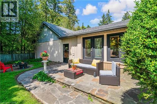 Flagstone patio with a raised section, featuring multiple large windows with dark trim, a side entry door, and a wood-paneled exterior - 91 Limerick Drive, Kitchener, ON - Outdoor
