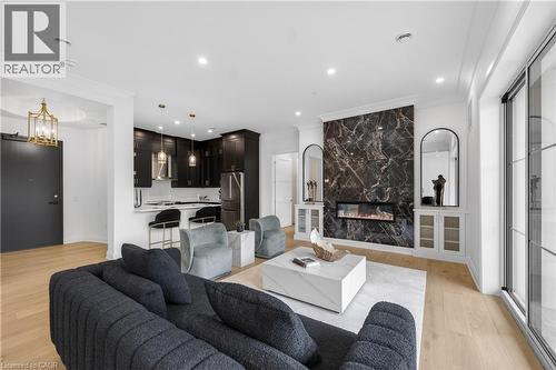 Open-concept living space featuring wood-finish flooring, a contemporary fireplace with a dark marble-effect surround, and built-in display cabinetry - 2 Arbourvale Common Unit# 410, St. Catharines, ON - Indoor Photo Showing Living Room With Fireplace
