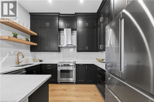 Modern kitchen featuring dark cabinetry, light countertops, stainless steel appliances, wood-finish flooring, and open shelving - 2 Arbourvale Common Unit# 410, St. Catharines, ON - Indoor Photo Showing Kitchen With Double Sink With Upgraded Kitchen