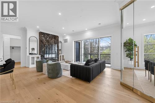 Spacious living area featuring a dark marble-clad fireplace, wood-finish flooring, recessed lighting, crown molding, and large glass sliding doors opening to an exterior balcony - 2 Arbourvale Common Unit# 410, St. Catharines, ON - Indoor Photo Showing Living Room