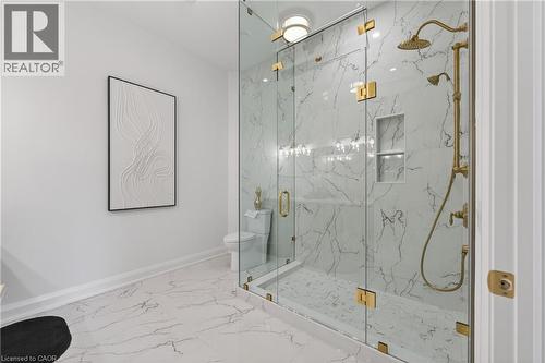 Glass-enclosed shower featuring large format white and gray veined tile, a built-in shower niche, and brass fixtures including a rain shower head and handheld shower sprayer - 2 Arbourvale Common Unit# 410, St. Catharines, ON - Indoor Photo Showing Bathroom