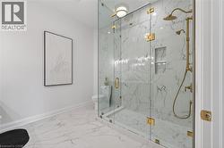 Glass-enclosed shower featuring large format white and gray veined tile, a built-in shower niche, and brass fixtures including a rain shower head and handheld shower sprayer - 