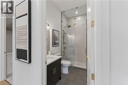 Bathroom featuring a glass-enclosed shower with gold-tone fixtures, a dark wood-finish vanity with a white countertop, and mosaic tile flooring - 2 Arbourvale Common Unit# 410, St. Catharines, ON - Indoor Photo Showing Bathroom