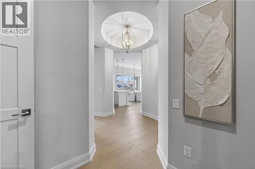 Hallway featuring wood-finish flooring, a tray ceiling with a hanging fixture, and white baseboards - 2 Arbourvale Common Unit# 410, St. Catharines, ON - Indoor Photo Showing Other Room