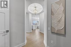 Hallway featuring wood-finish flooring, a tray ceiling with a hanging fixture, and white baseboards - 