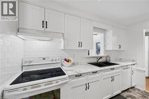Kitchen featuring white beadboard cabinetry with black hardware, white subway tile backsplash, light-toned countertop, and a double basin sink - 50 Lewis Crescent, Kitchener, ON - Indoor Photo Showing Kitchen With Double Sink