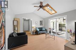 Vaulted ceiling living area featuring a skylight, ceiling fan, wood-finish flooring, and sliding glass doors opening to a stone patio - 