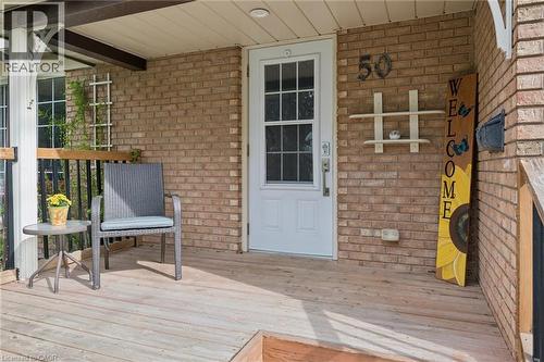Brick exterior with a covered porch featuring a white entry door with glass inserts, a wood-finish deck, and black metal railings - 50 Lewis Crescent, Kitchener, ON - Outdoor With Deck Patio Veranda With Exterior