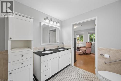 Bathroom featuring a dual-sink vanity with a dark countertop and white cabinetry, a built-in linen tower, white tile flooring, and a tiled half-wall - 50 Lewis Crescent, Kitchener, ON - Indoor Photo Showing Bathroom