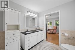 Bathroom featuring a dual-sink vanity with a dark countertop and white cabinetry, a built-in linen tower, white tile flooring, and a tiled half-wall - 