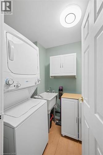 Dedicated laundry space featuring a stacked washer and dryer, utility sink with chrome faucet, white cabinetry, and wood-finish flooring - 50 Lewis Crescent, Kitchener, ON - Indoor Photo Showing Laundry Room