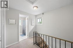 Upper landing featuring light-toned carpeting, a window with white trim, and a metal staircase railing - 
