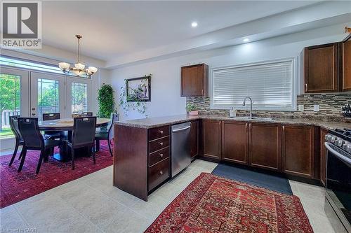 Kitchen featuring wood-finish cabinetry, stainless steel dishwasher, and a mosaic tile backsplash - 197 Cloverleaf Drive, Ancaster, ON - Indoor