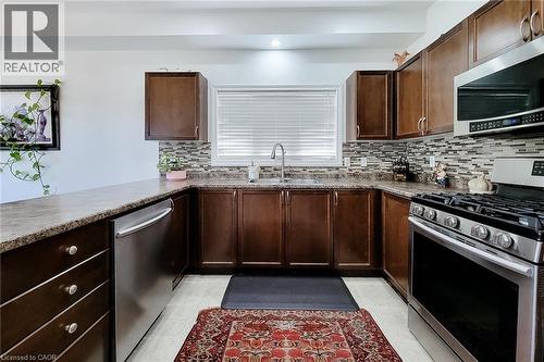 U-shaped kitchen featuring wood-finish cabinetry and granite-pattern countertops - 197 Cloverleaf Drive, Ancaster, ON - Indoor Photo Showing Kitchen With Double Sink