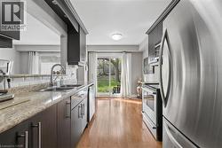 Modern kitchen featuring a double basin sink, light-colored countertops, subway tile backsplash, dark wood-finish cabinetry with silver hardware, and stainless steel appliances - 