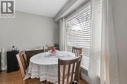 Dining area with light gray walls, wood-finish flooring, a large window with blinds, and sheer white curtains - 